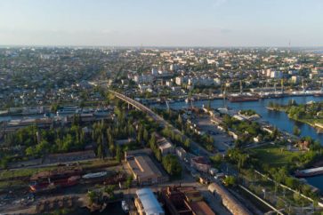 Aerial view of the Kherson city. A shipyard on the banks of the Dnieper River of which there are cranes and ships. Residential area with houses and greenery