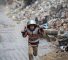 TOPSHOT - A displaced boy covers his head with a pan as he runs from the rain past building rubble at the Bureij refugee camp in the central Gaza Strip on November 24, 2024, amid the ongoing war between Israel and the Palestinian Hamas militant group. (Photo by Eyad BABA / AFP)