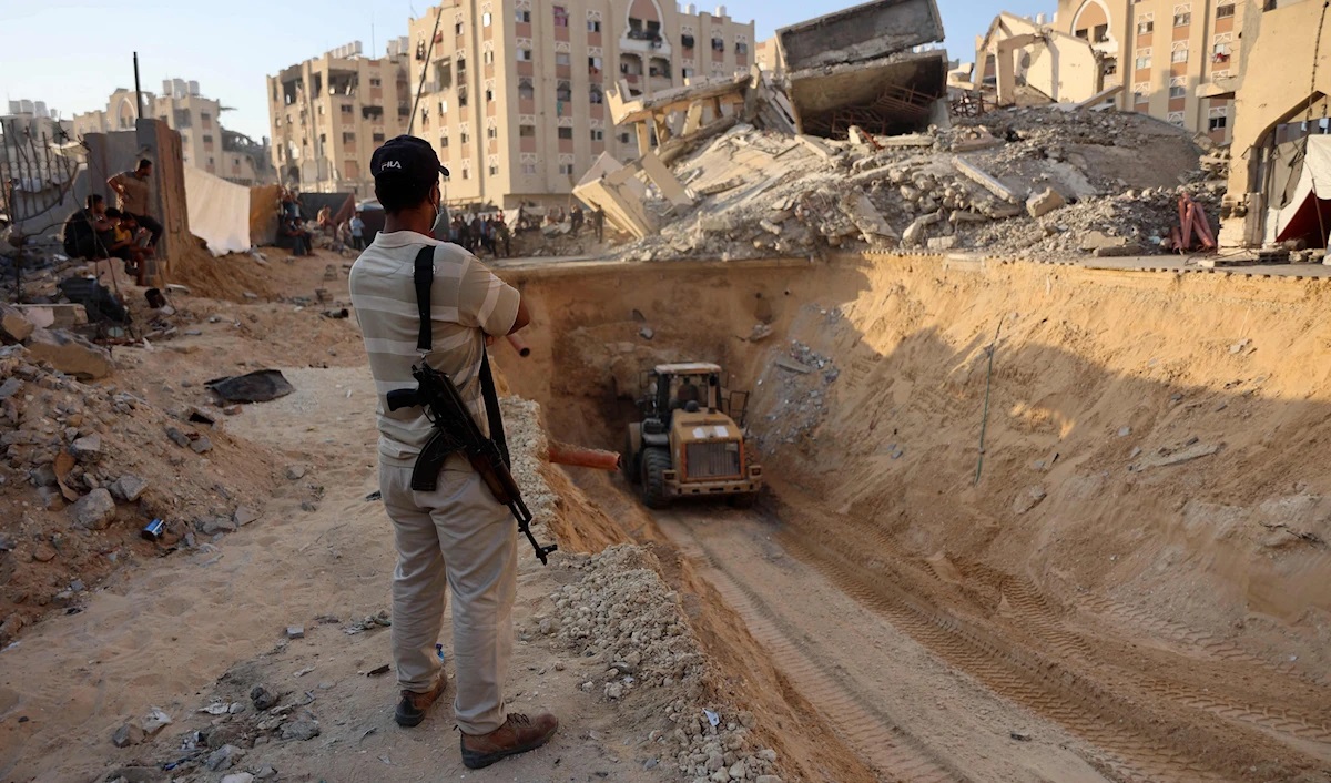 Un combatiente de la resistencia palestina observa una excavadora mientras excava en busca de cuerpos de prisioneros israelíes en Jan Yunis (AFP)